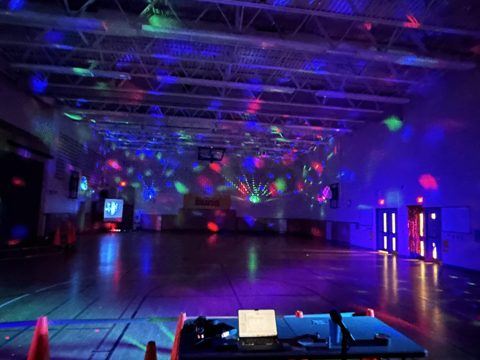 A school gym lit purple with disco lights for a dance, set up and ready before the students arrive