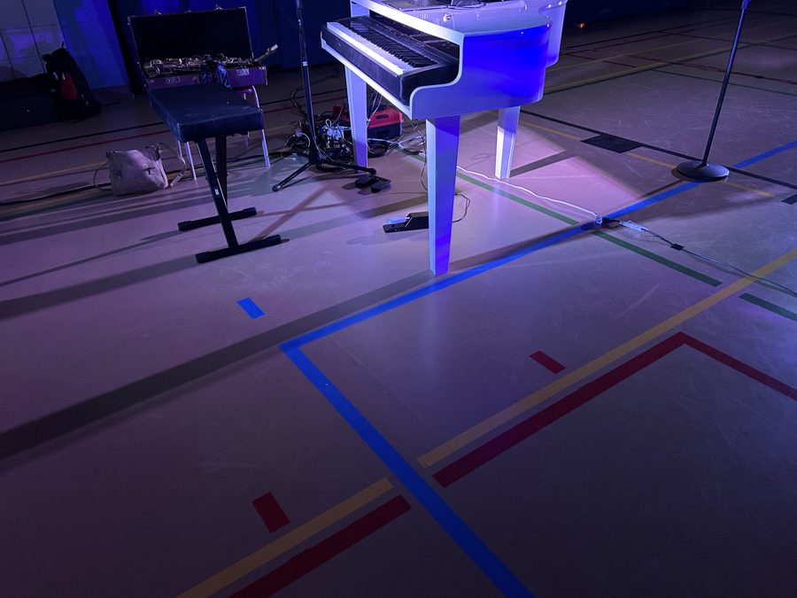 The same kind of gym after setup: white piano, keyboard and speakers at the stage end