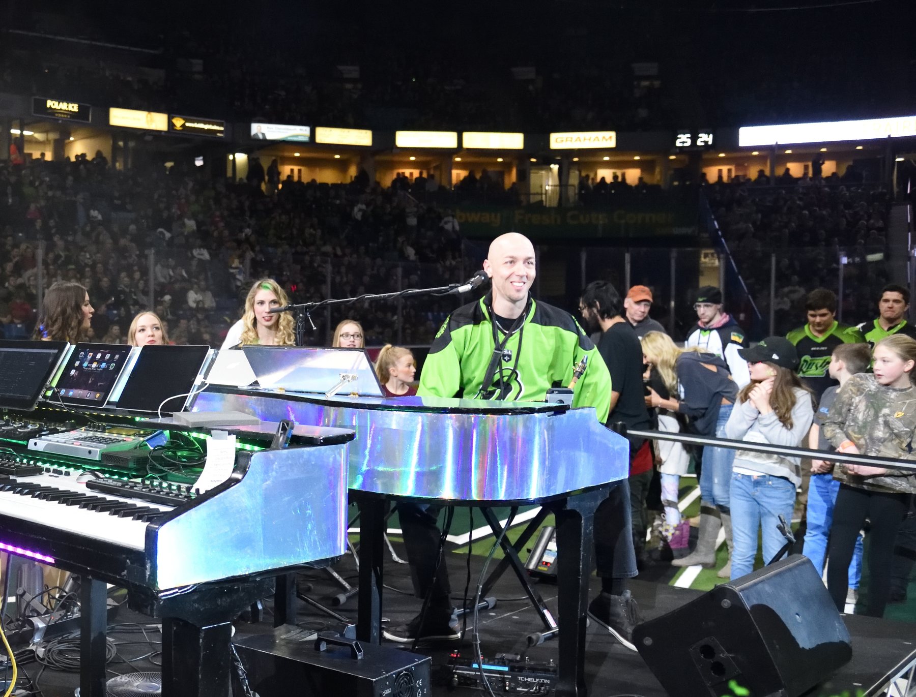 A lit piano on a stage in front of a packed stadium crowd.